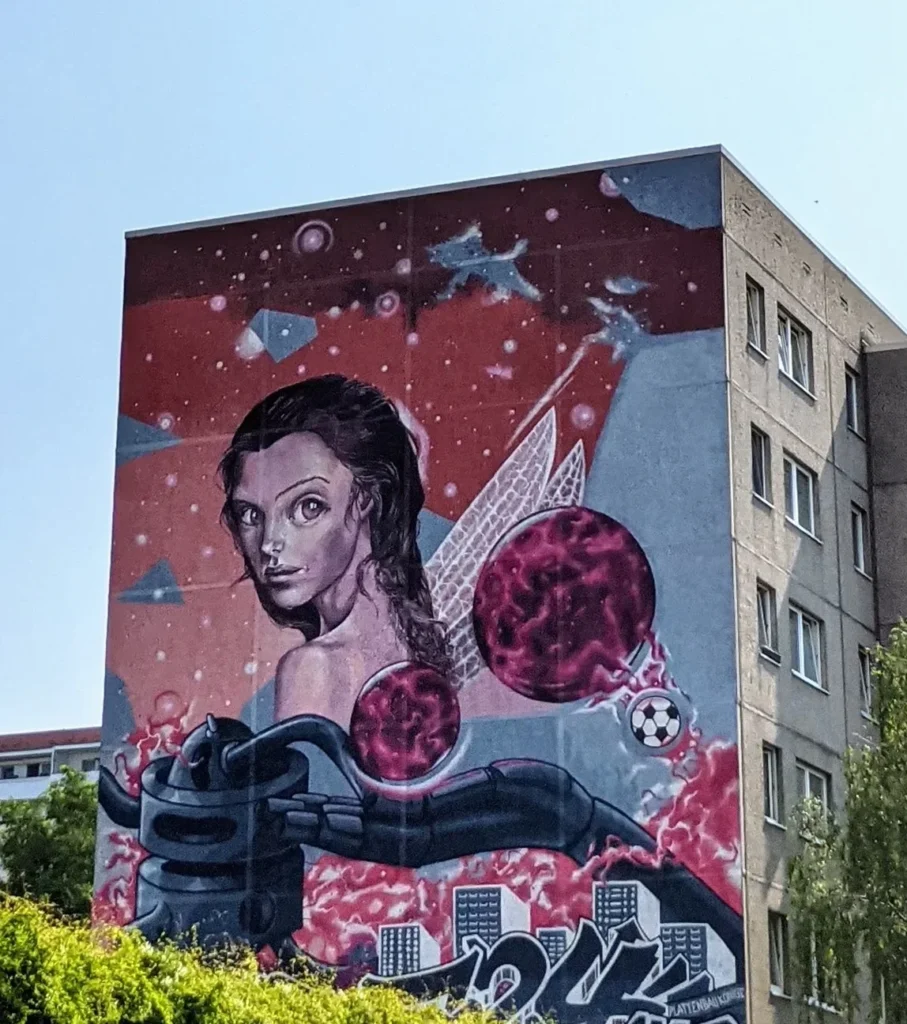 Wandbild von Age Age, Akte One und Caro Pepe an einem Plattenbau in Berlin-Altglienicke: junge Frau mit Zopf und Flügeln vor rotem Grund