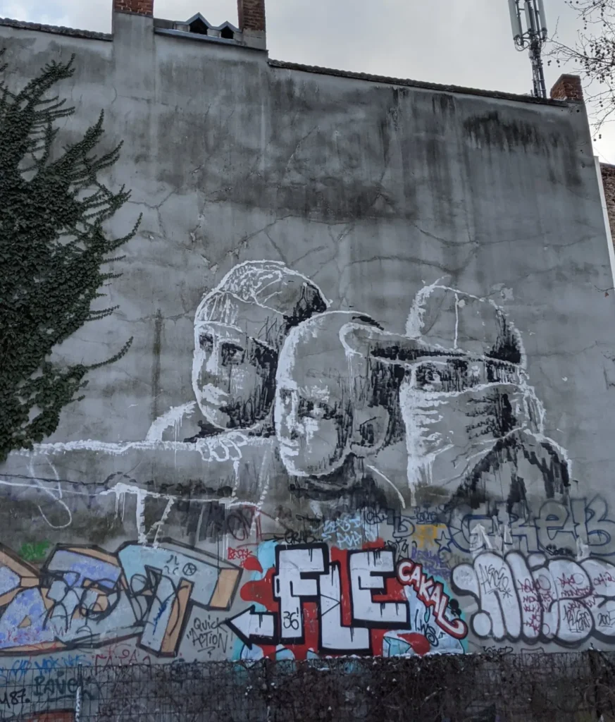 Wandbild No child is born a criminal von Alaniz im Wrangelkiez in Berlin-Kreuzberg: drei Kinder mit Mützen und Tüchern vor dem Gesicht auf grauer Wand