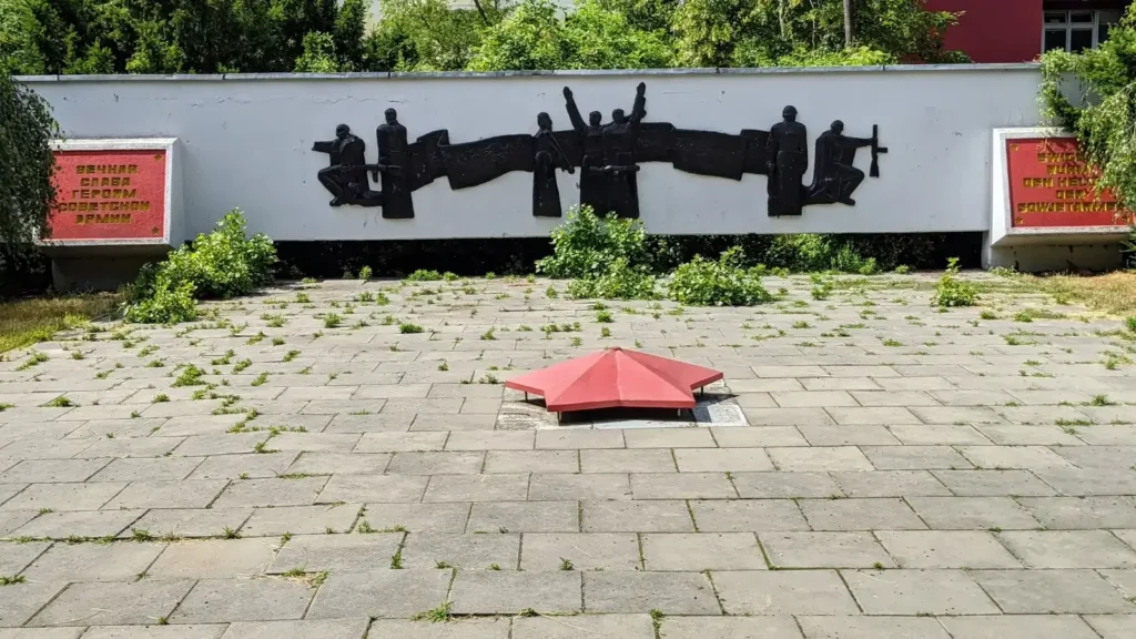 Weiße Wand mit schwarzem Relief des Sowjetischen Ehrenmals in Alt-Hohenschönhausen, davor roter Stern im Boden