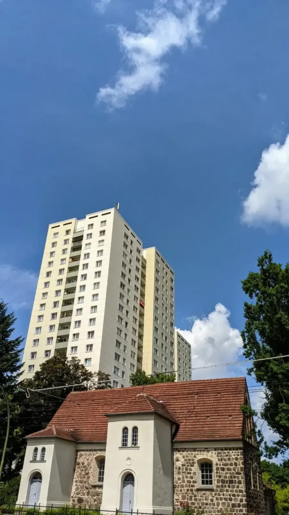 Feldsteinkirche Taborkirche an der Hauptstraße in Alt-Hohenschönhausen, dahinter ein Hochhaus in Plattenbauweise
