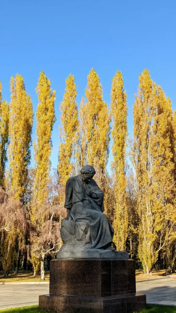 Sitzende Steinfigur Mutter Heimat im Vorhof des Sowjetischen Ehrenmals im Treptower Park, dahinter Pappeln