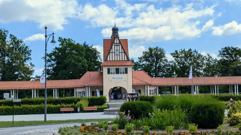 Bahnhof Bad Saarow mit Fachwerkturm und langen Kolonnaden, davor Blumenbeete