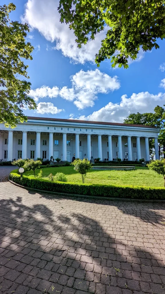 Säulenhalle des Badehauses Goor bei Lauterbach mit Rasen und Kugelbäumchen davor, im Hochformat