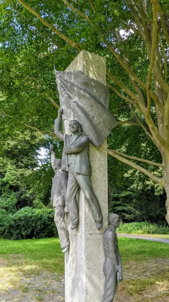 Gedenkstele mit vier Bronzefiguren und Fahne von Gerhard Thieme am Eingang des neuen Friedhofs Baumschulenweg