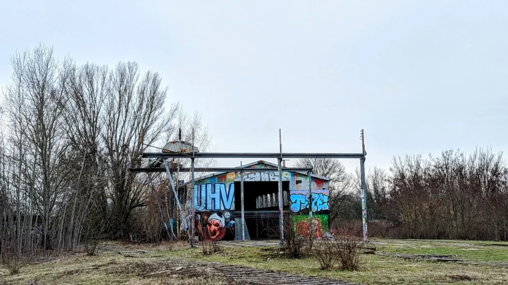 Kleines Häuschen mit Graffiti hinter einem Zaun am Rand des Biesenhorster Sands