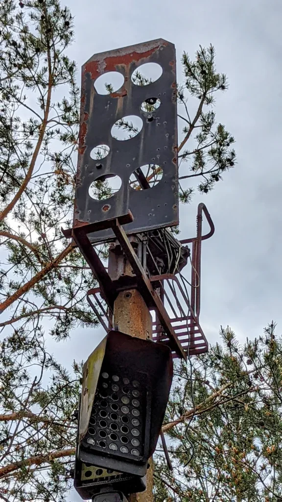 Rostiger Signalschirm mit runden Öffnungen an einem Mast vor Kiefernzweigen
