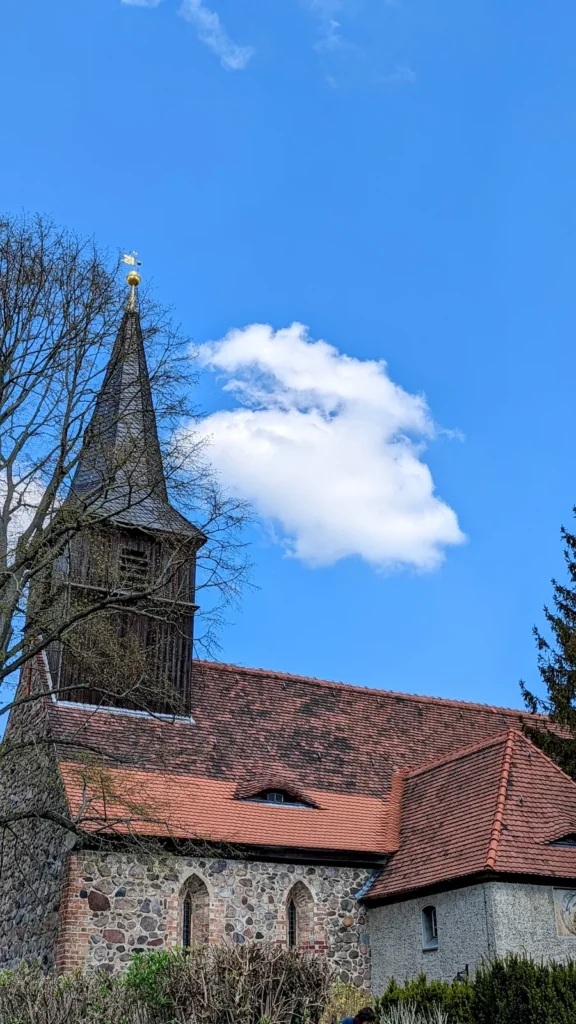 Feldsteinkirche mit rotem Ziegeldach und hölzernem Turm der Dorfkirche Blankenfelde unter blauem Himmel