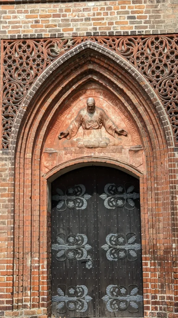 Gotisches Backsteinportal der St. Gotthardtkirche in Brandenburg an der Havel mit Maßwerkfries und Christusrelief im Bogenfeld