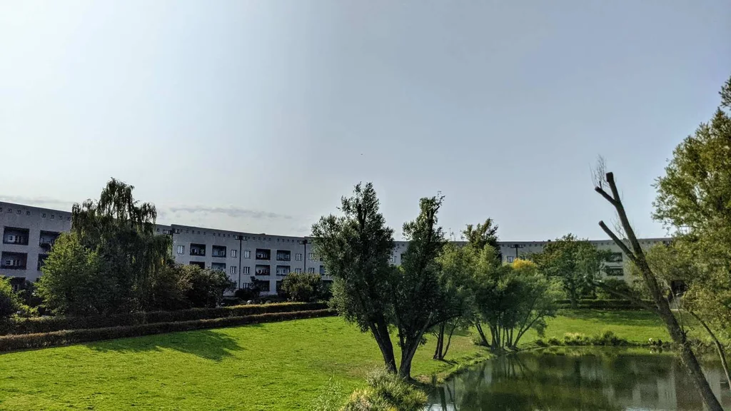 Hufeisenförmiger Wohnblock der Hufeisensiedlung in Britz hinter Wiese und Teich