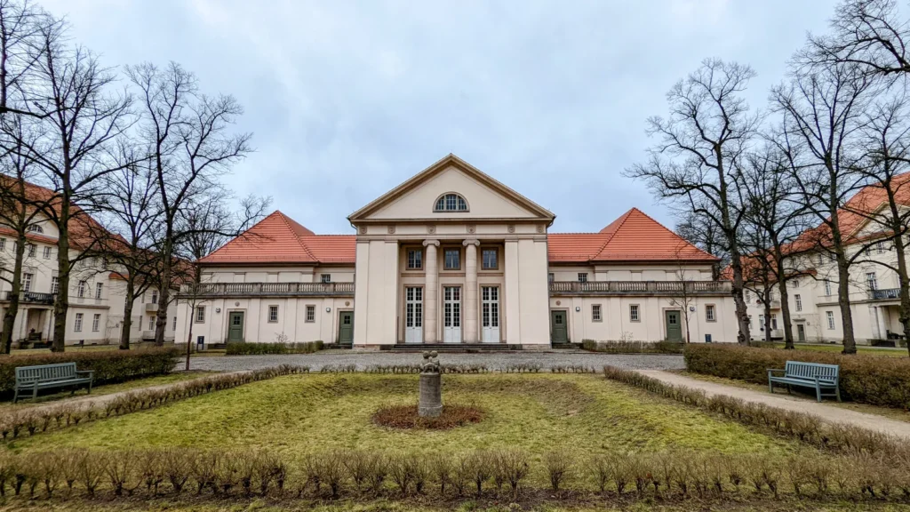 Symmetrischer Putzbau mit Säulenportikus, rotem Dach und gepflegter Rasenfläche im früheren Klinikareal von Buch