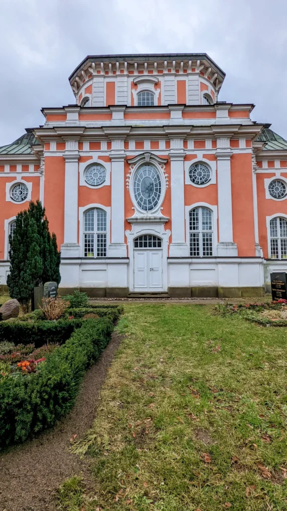 Barocke Schlosskirche Buch mit orangeroter Fassade, Portal und Kuppelaufsatz ohne Turm, davor Buchsbeete
