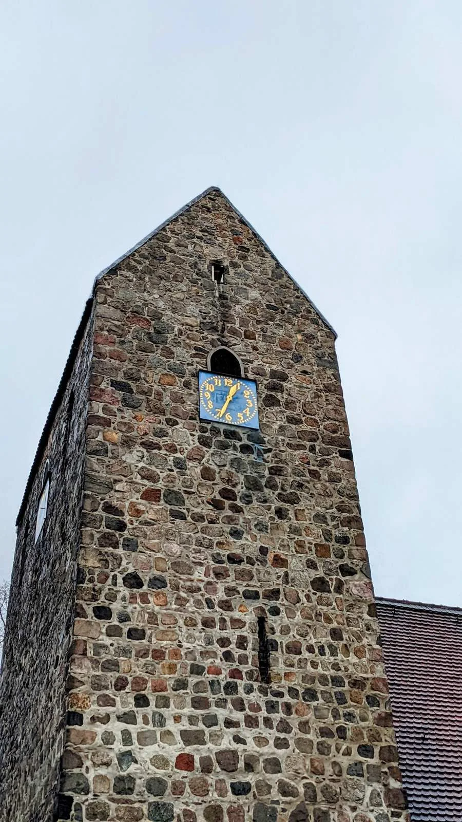 Feldsteinturm der Dorfkirche Alt-Buckow mit blauer Turmuhr, von unten gesehen