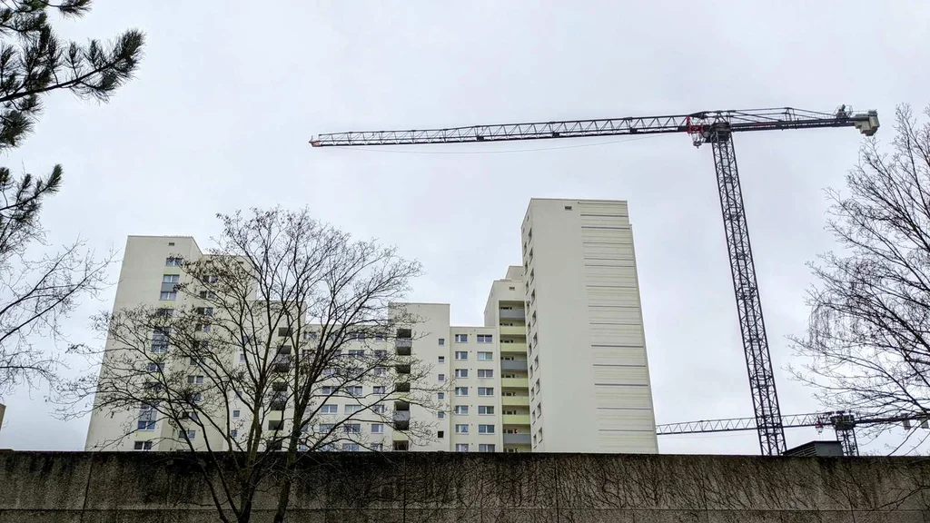 Helle Wohnhochhäuser hinter einer Betonmauer, rechts ein Baukran, im Ortsteil Buckow in Neukölln