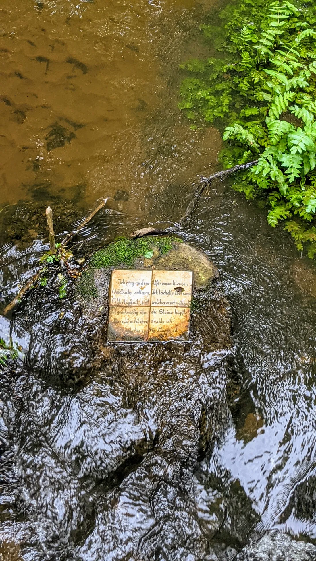 Kachel mit Text auf einem Stein im Bach in Rädigke