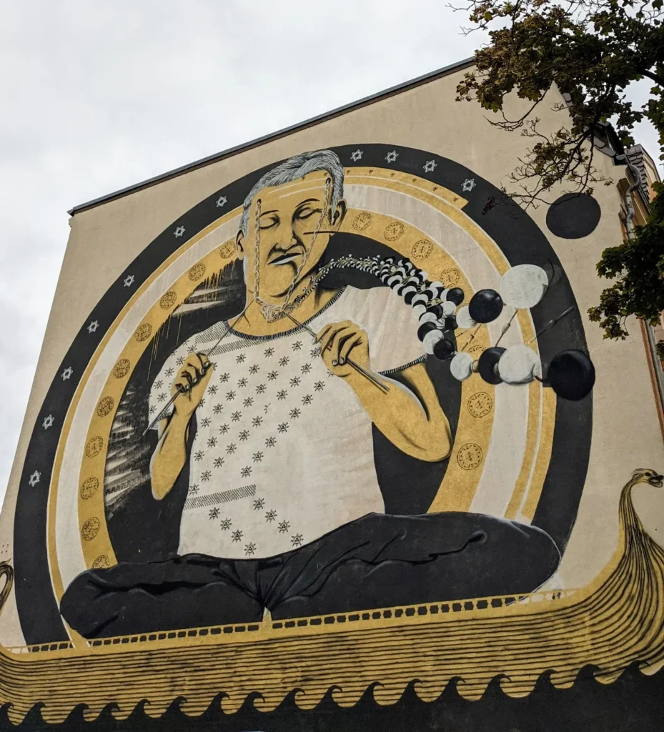 Wandbild von Captain Borderline an der Geschwister-Scholl-Straße in Lutherstadt Wittenberg: sitzender Mann in goldenem Kreis über einer verzierten Bootsform