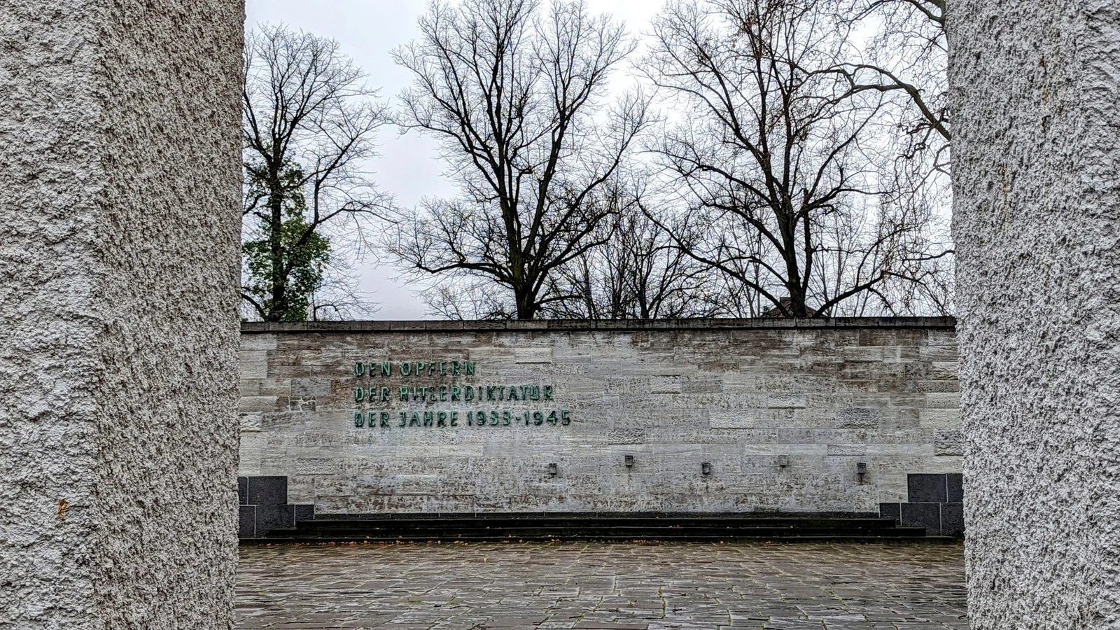Gedenkmauer mit Inschrift am Eingang der Gedenkstätte Plötzensee, dahinter kahle Bäume