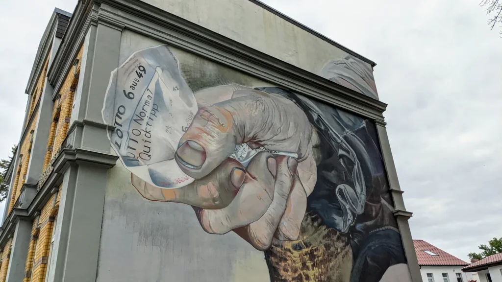 Wandbild an einer Giebelwand in Lutherstadt Wittenberg: eine große Hand hält einen Lottoschein „6 aus 49“
