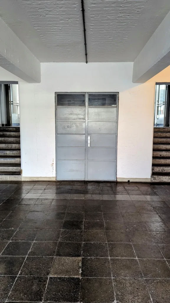 Innenraum im Bauhausgebäude in Dessau mit dunklem Fliesenboden, zwei Treppen und einer Glastür