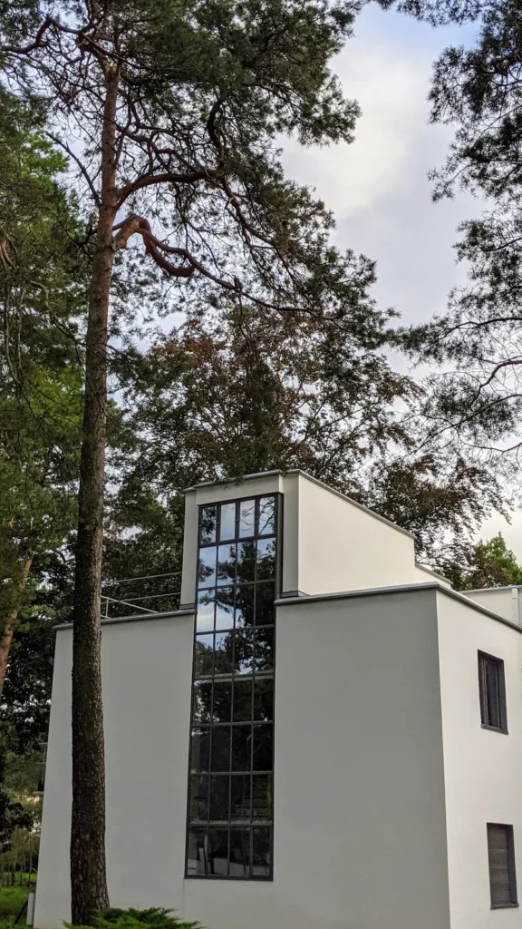 Weißer Baukörper eines Meisterhauses in Dessau mit hohem Glasstreifen zwischen Kiefern