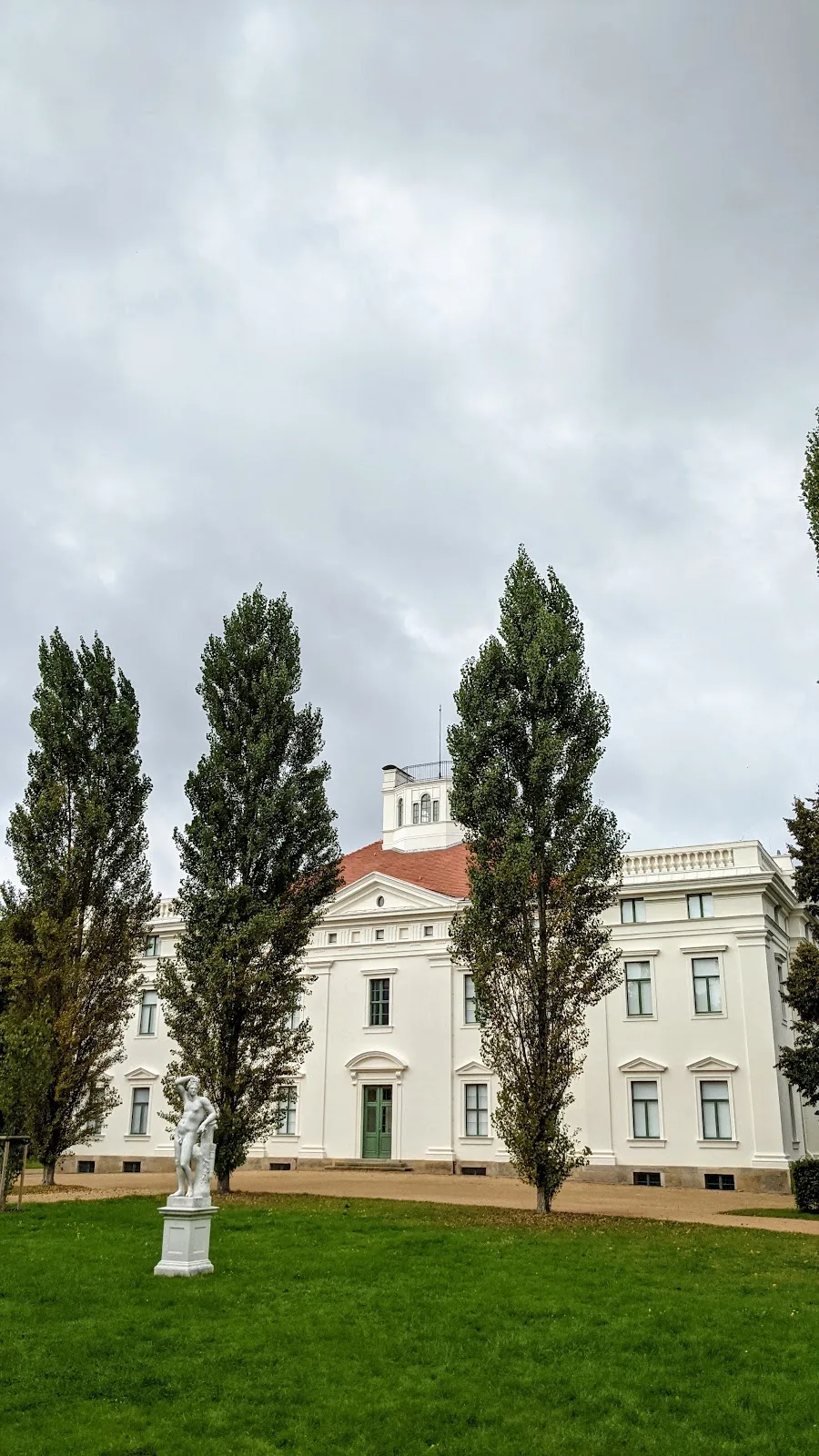 Weißes Schloss Georgium in Dessau hinter Pyramidenpappeln, davor eine Statue auf dem Rasen