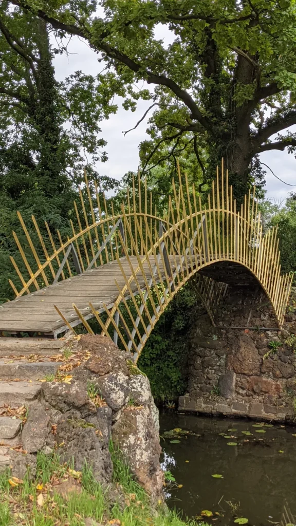 Brücke mit goldfarbenem Stabgeländer über einem Bogen aus Bruchstein im Wörlitzer Park