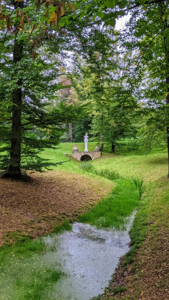 Graben im Park Luisium, hinten eine kleine Brücke mit weißer Figur