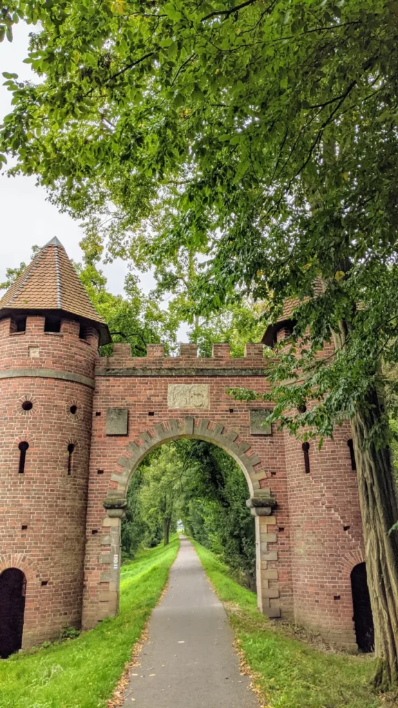 Backsteintor mit zwei runden Türmen und Zinnen am Waldpark Sieglitzer Berg, ein Radweg führt hindurch
