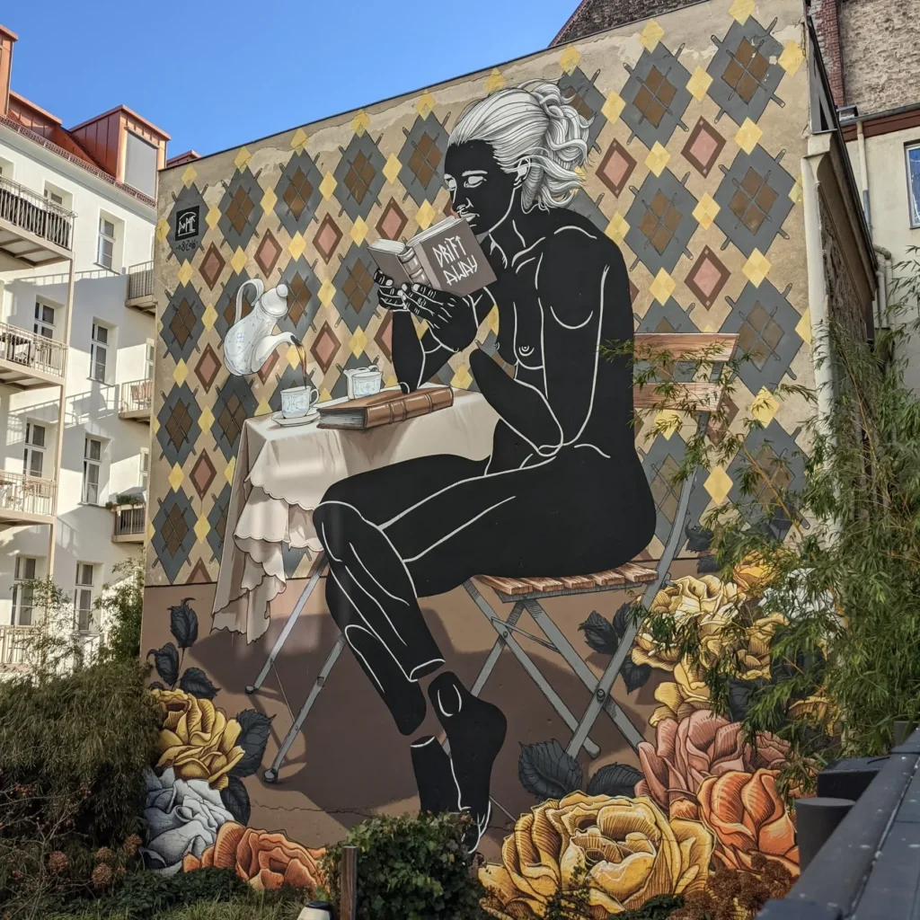Wandbild Tea Time! an der Bleibtreustraße in Berlin-Charlottenburg: schwarze Frauenfigur mit Buch am Teetisch vor einem Rautenmuster, unten gemalte Rosen