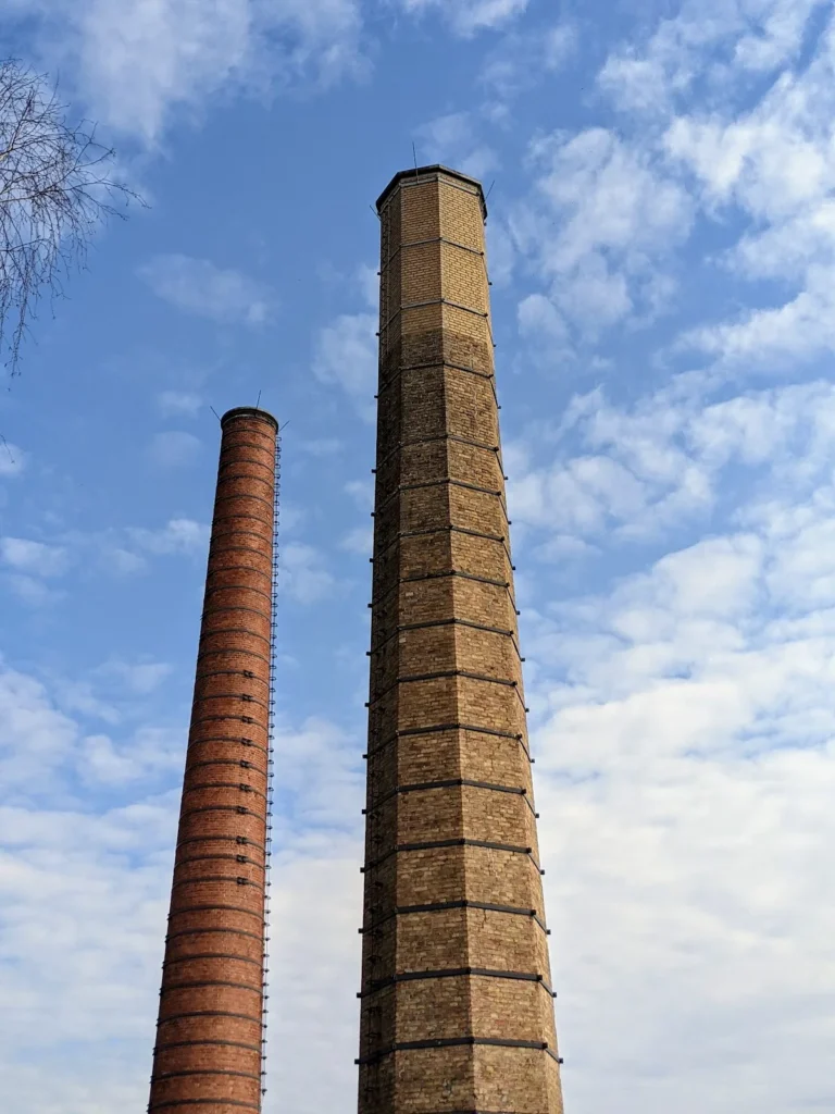 Zwei Backsteinschornsteine in Eberswalde, einer rot und einer gelblich, vor blauem Himmel