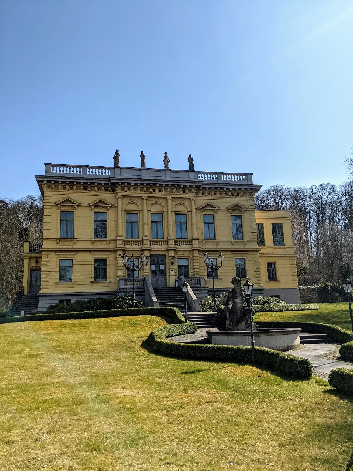 Märchenvilla in Eberswalde, gelb verputzte Villa mit Figuren auf der Balustrade und Brunnen im Garten