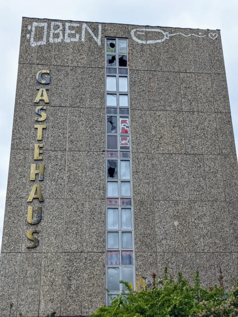 Fensterloser Giebel eines leerstehenden Hochhauses mit senkrechtem Schriftzug Gästehaus und einem Graffito am oberen Rand