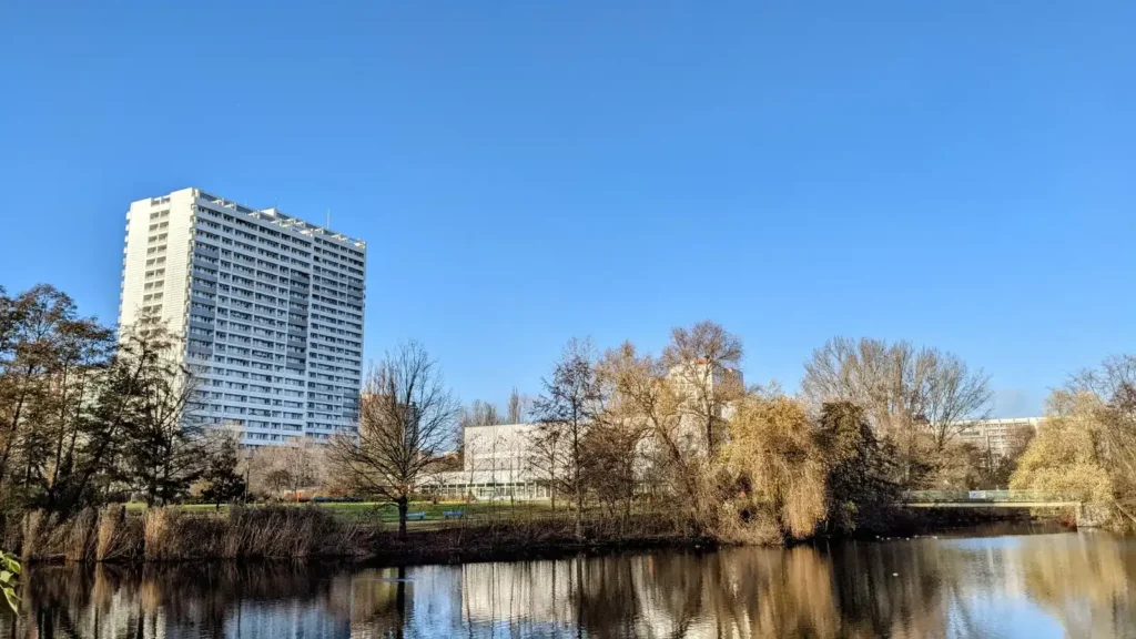 Der Fennpfuhl im Fennpfuhlpark im Herbst, dahinter ein Hochhaus der Großsiedlung
