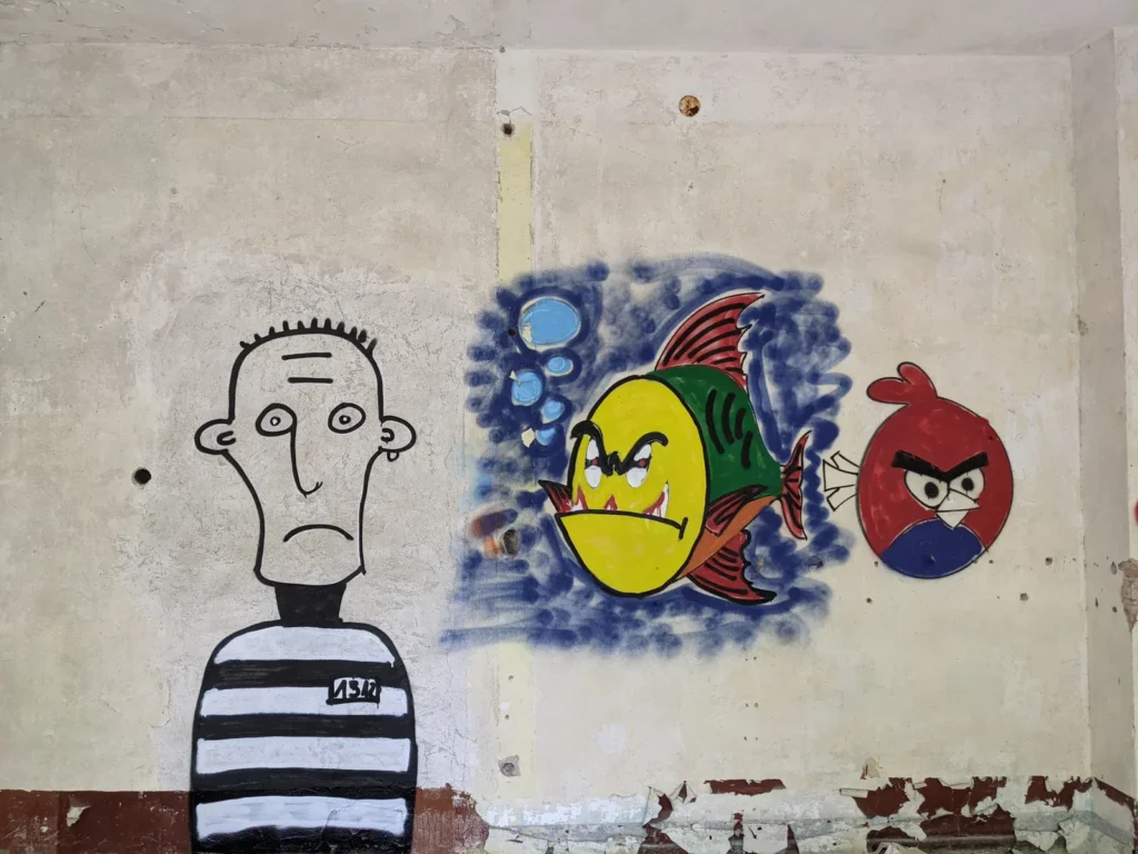 Graffiti mit gestreifter Figur, Fisch und Angry-Birds-Vogel auf dem Gelände bei Brand
