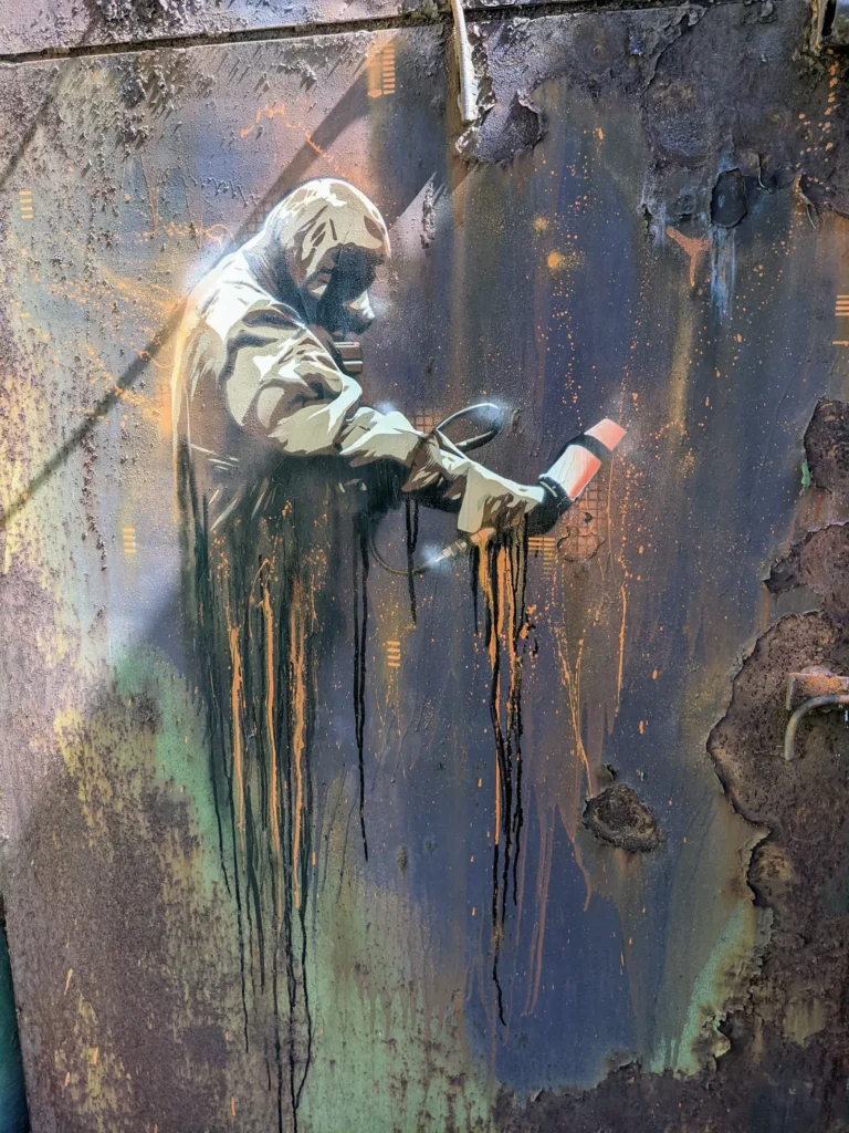 Graffito einer Figur im Schutzanzug mit Sprühdose auf dem Gelände bei Brand