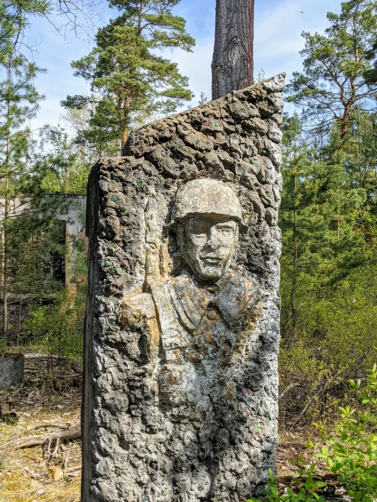 Soldatenplastik mit Helm als Relief an einer Stele aus Kieselbeton im Wald bei Brand
