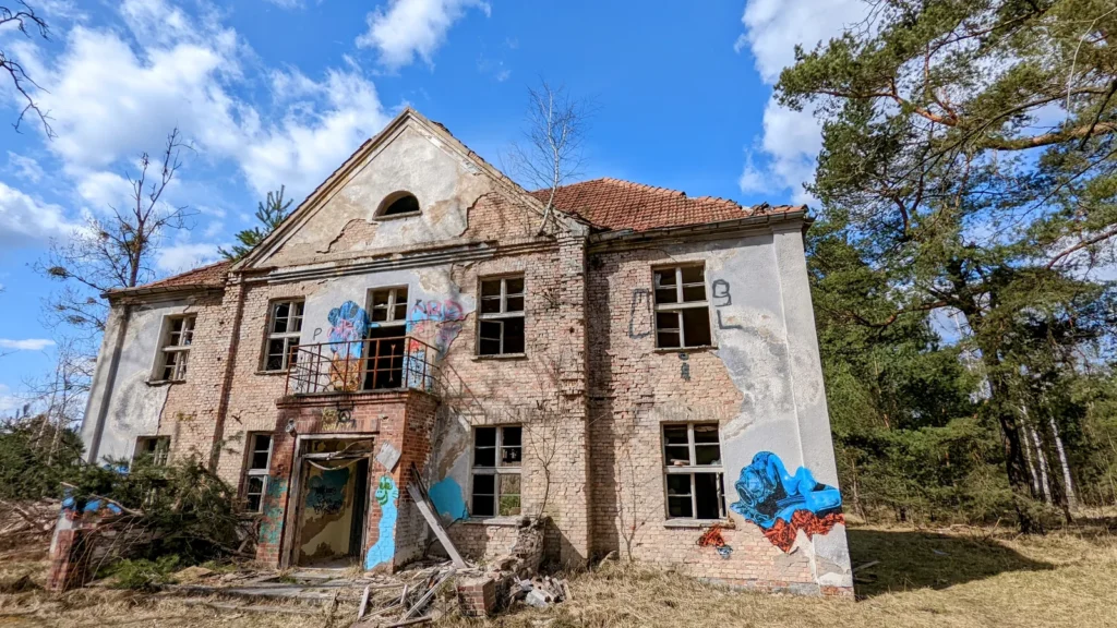 Zweigeschossiges Backsteinhaus mit leeren Fenstern und Graffiti unter Wolkenhimmel