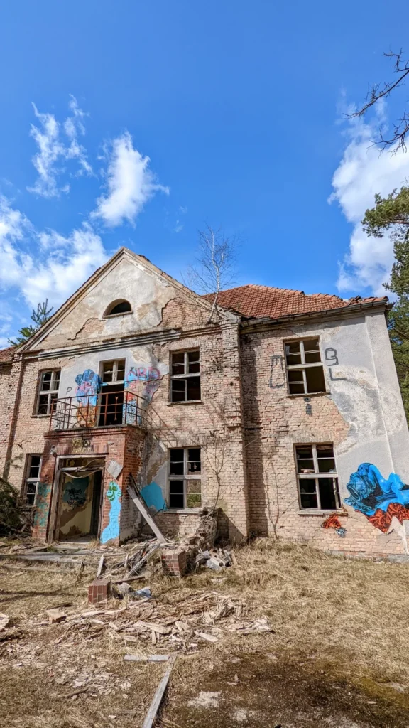 Zweigeschossiges Backsteinhaus mit leeren Fenstern und Graffiti unter blauem Himmel