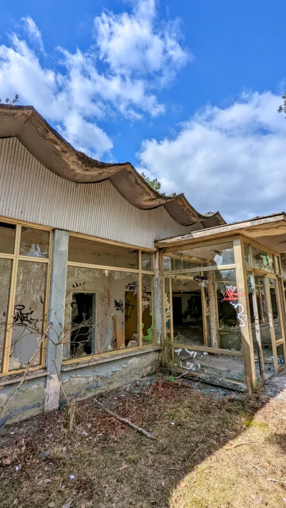 Flachbau mit Fensterfront und wellenförmigem Dach unter Wolkenhimmel