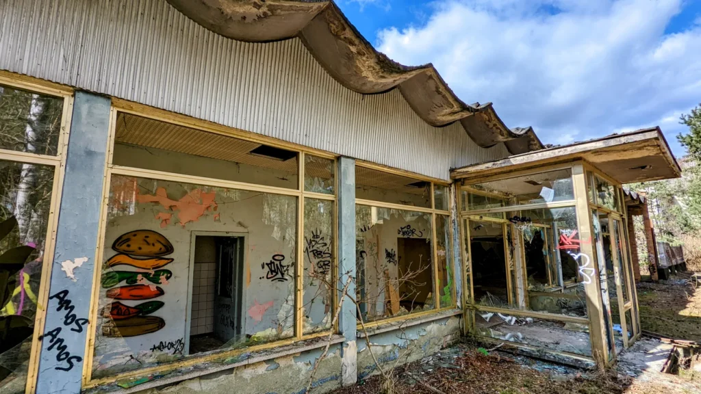 Flachbau mit Fensterfront und wellenförmigem Dach, Graffiti hinter den Scheiben