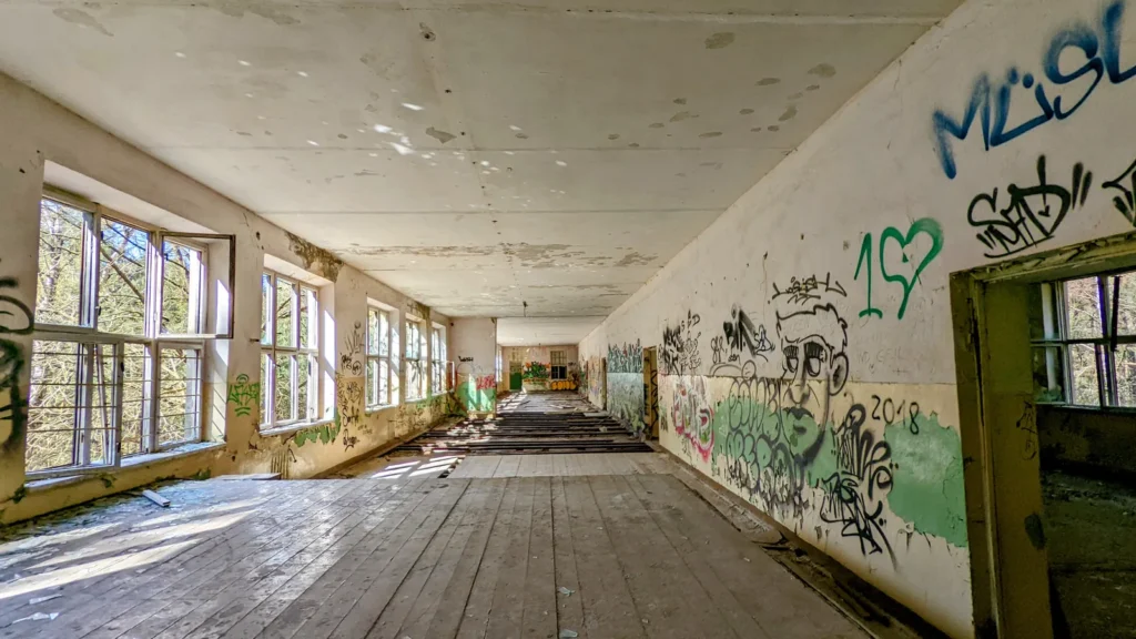 Langer Raum mit Dielenboden, Fensterreihe links und Graffiti an der rechten Wand