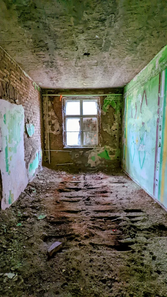 Schmaler Raum mit grünen Wänden, Fenster am Ende und Schutt auf dem Boden