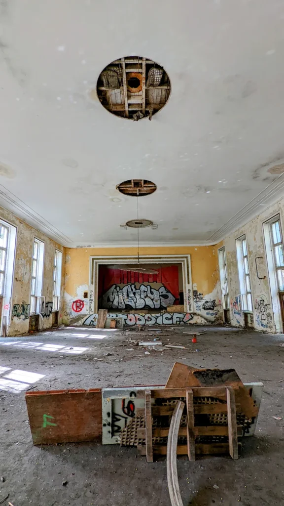 Großer Saal mit Bühne am Ende, Graffiti und umgekippter Holzkonstruktion