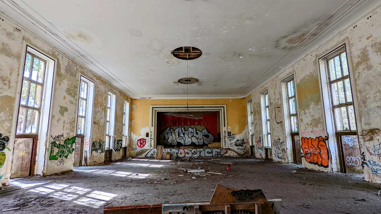 Großer Saal mit hohen Fenstern und Bühne mit rotem Vorhang