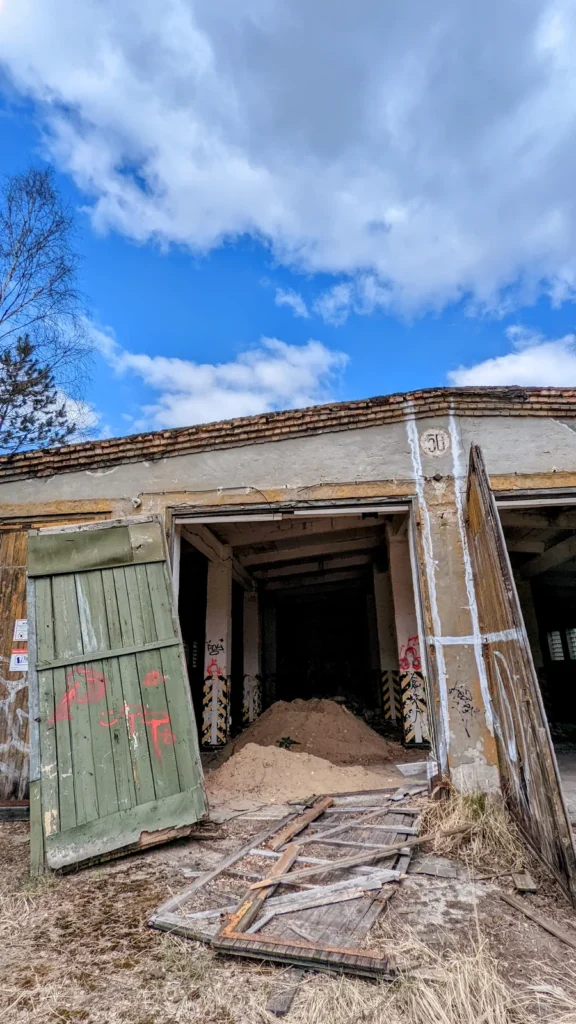 Flachbau mit geöffnetem Tor, grünem Torflügel und Holzspänen davor