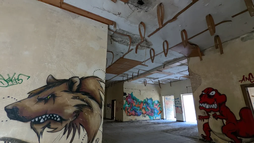 Halle mit Graffiti: Tierkopf mit Zähnen links, rote Figur rechts, Holzträger an der Decke
