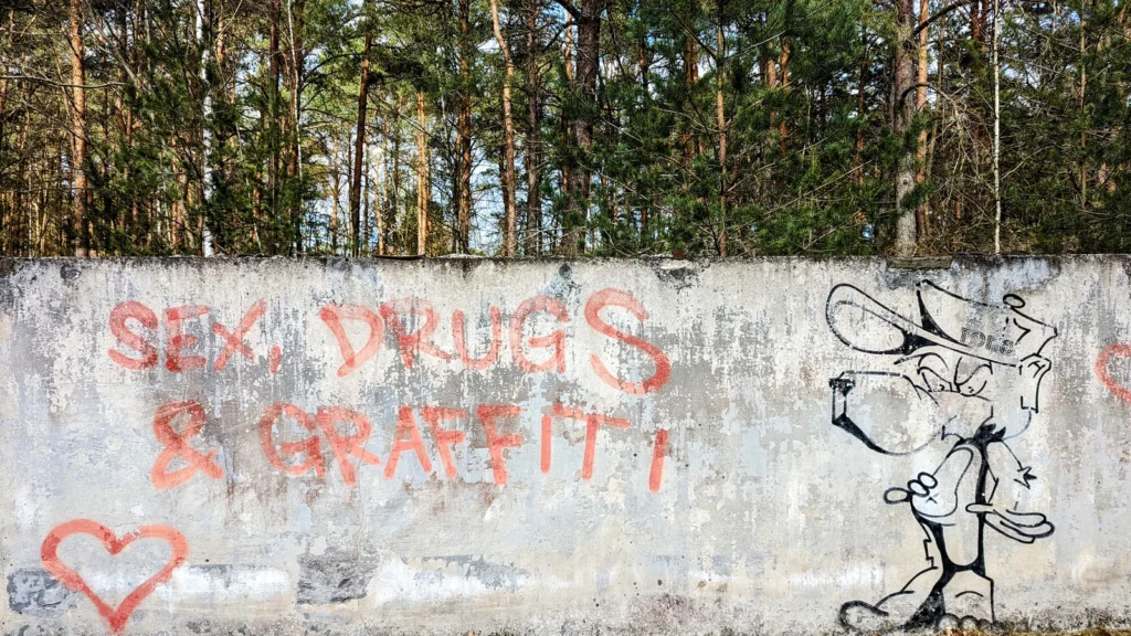 Betonwand im Wald mit Graffiti „Sex, Drugs & Graffiti“, Herz und schwarzer Tierfigur