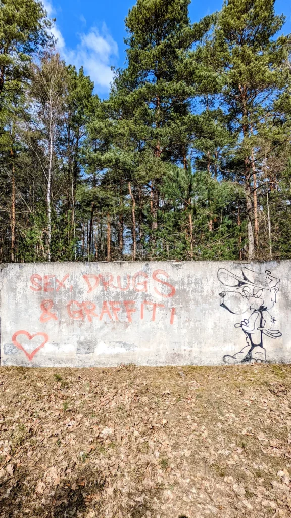 Betonwand zwischen Waldbäumen mit Graffiti und schwarzer Figur