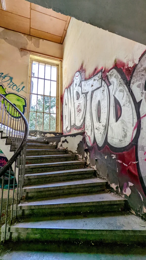 Treppenhaus mit Wendelgeländer, Graffiti und hohem Fenster