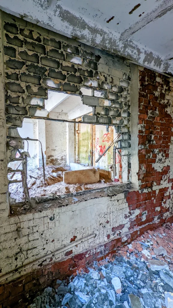 Wand mit Durchbruch und Blick in einen Raum, davor Schutt