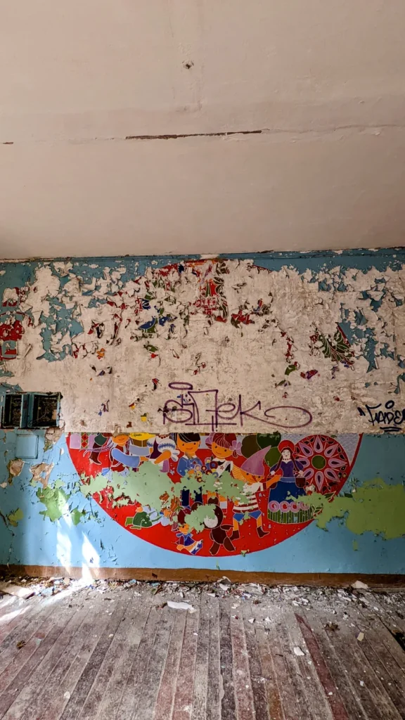 Raum mit bemalter Wand, rotem Halbkreis mit bunten Figuren und Holzdielen